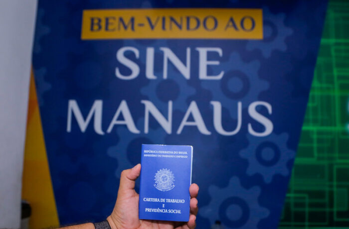 Carteira de trabalho em frente a um painel do Sine Manaus