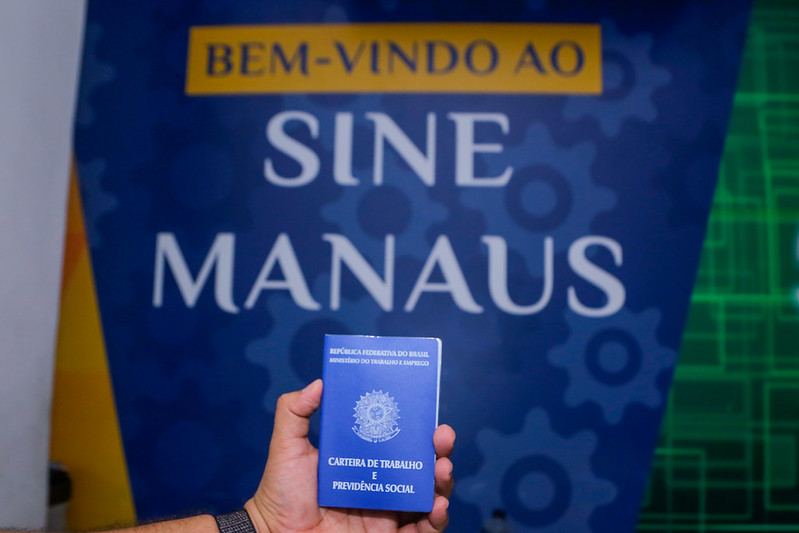 Carteira de trabalho em frente a um painel do Sine Manaus